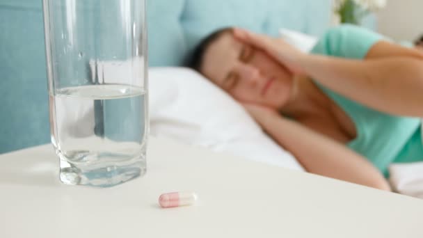 4 k felvétel, fiatal beteg asszony feküdt az ágyban, véve pirulát éjjeliszekrény és pohár vizet inni — Stock videók
