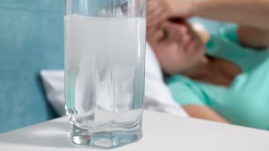 Aspirin ilaç başucundaki kadın yatakta yatan baş ağrısı muzdarip karşı eriterek ile su görüntülerini closeup 4k
