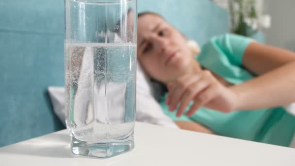 4 k close-up video van jonge vrouw lijdt aan hoofd pijn in bed liggen en drinken aspirine in glas — Stockvideo