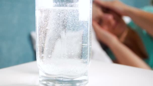 Vidéo en gros plan au ralenti de bulles d'air provenant d'une tablette d'aspirine coulant dans un verre d'eau. Femme avec migraine couchée au lit — Video
