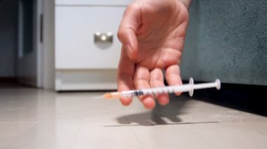 Evde yere düşen şırınga tutarak el closeup ağır çekim görüntüleri. Uyuşturucu ve uyuşturucu bağımlılığı kavramı