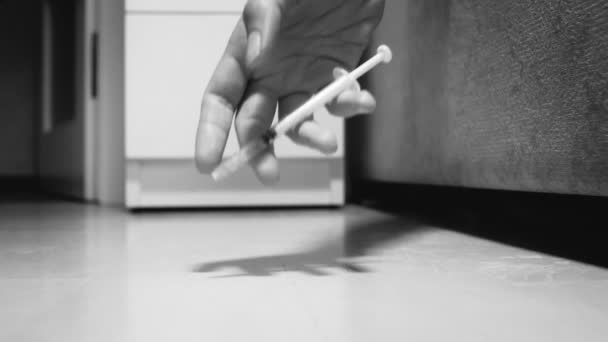 Black and white closeup footage of syringe slowly falling out of female hand on floor. Concept of drugs and narcotics addiction — Stock Video