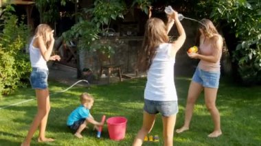 mutlu genç aile sıçramasına ve birbirlerine üzerine su dökerek sıcak güneşli gün arka bahçe çim üzerinde 4 k video