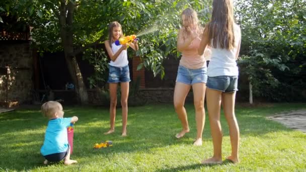 Imágenes de 4k de la familia feliz divirtiéndose en la hierba en el patio trasero y disparando con agua de pistolas de juguete — Vídeo de stock