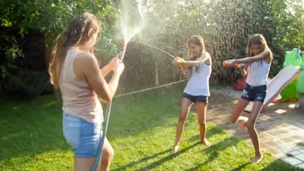 4k кадров, где молодая мать брызгает водой из садового шланга на свою дочь игрушечными пушками — стоковое видео