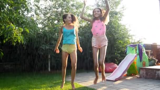 Imágenes de 4k de dos adolescentes disfrutando de la lluvia en el caluroso día de verano en el patio trasero — Vídeos de Stock