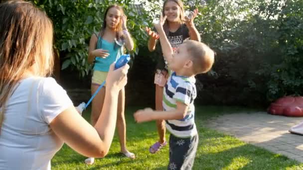 4k видео счастливых смеющихся детей, преследующих и ловящих летящие мыльные пузыри на заднем дворе дома — стоковое видео