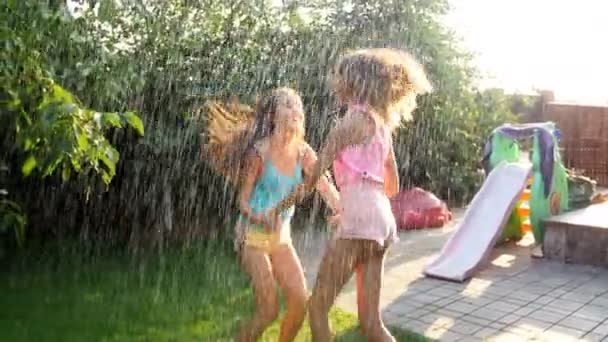 4k video of two teenage girls dancing and jumping under water splashing from garden hose at backyard — Stock Video