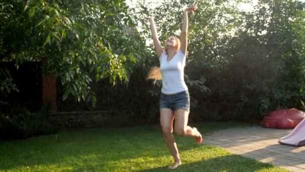 4k metraje de risa alegre joven bailando bajo la lluvia de verano en la puesta de sol en el patio trasero de la casa — Vídeo de stock