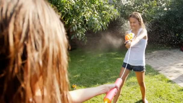 Pomalu mtoion footag eof dvě dospívající dívky hrát s vodní děla na trávě na zahradě — Stock video