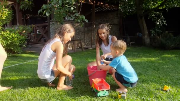 Slow-motion video van gelukkige kinderen vullen speelgoed water guns uit emmer in achtertuin — Stockvideo