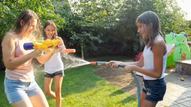 Vídeo en cámara lenta de la niña rociando agua de la manguera del jardín sobre su madre y su hermana mayor en el día soleado caliente — Vídeos de Stock