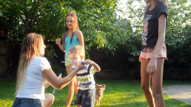 Slow motion bilder av bedårande barn pojken blåser såpbubblor med familj på gräs på bakgården — Stockvideo