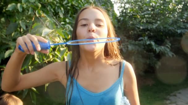 Vídeo em câmera lenta de menina morena sorridente feliz soprando bolhas de sabão no parque no dia ensolarado — Vídeo de Stock