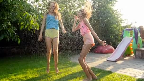 Vídeo em câmera lenta de duas gargalhadas adolescentes desfrutando de chuva de verão na grama no quintal — Vídeo de Stock