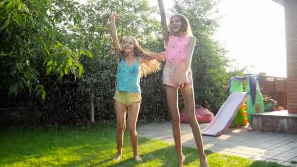 Zeitlupenvideo von zwei lachenden Teenagerinnen, die bei Sonnenuntergang im Sommerregen springen und tanzen — Stockvideo
