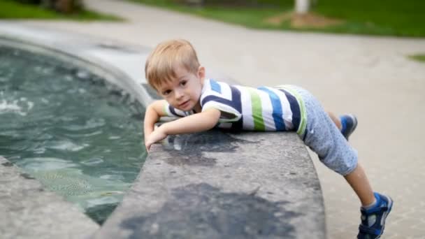 4k metraje de lindo niño tocando el agua en la fuente en el parque — Vídeos de Stock