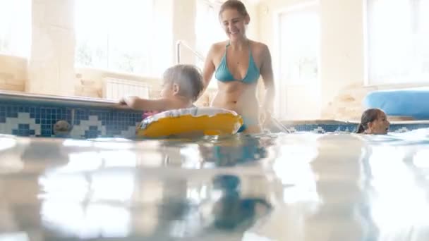 4k 视频小学步男孩游泳充气环与母亲在室内游泳池 — 图库视频影像