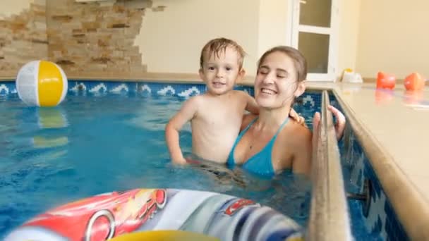 4k video de adorable sonriente niño pequeño con la madre nadando en la piscina una casa — Vídeo de stock