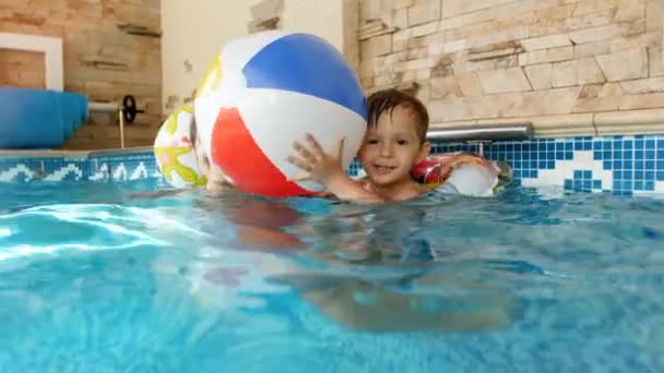 4k vídeo de feliz lauhging criança menino no anel inflável brincando com a mãe e jogando colorido bola de praia na piscina — Vídeo de Stock