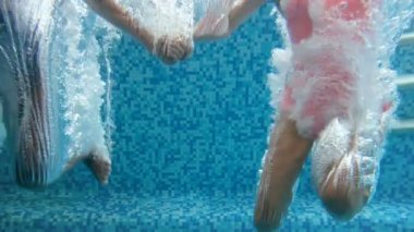 Yavaş hareket sualtı görüntüleri iki kız su altında dalış ve yüzme havuzunda atlama elele. Yavaş yavaş yukarı kaldırarak hava kabarcıkları.