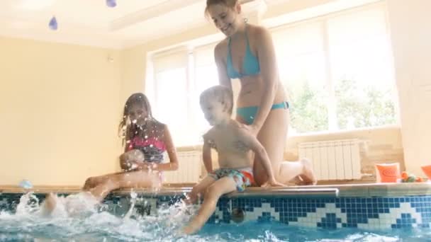 4k video de adorable niño sentado en la piscina con adolescente y salpicaduras de agua con los pies — Vídeo de stock