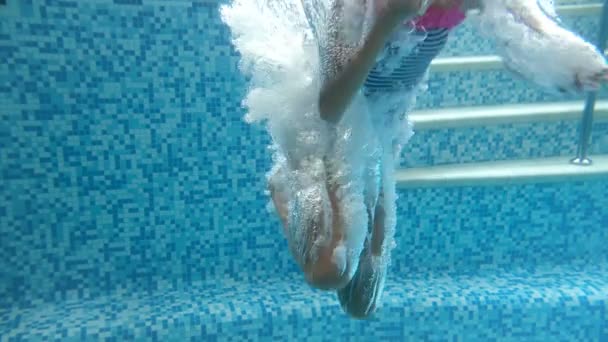 Vídeo subacuático en cámara lenta de una adolescente en traje de baño a rayas con gafas saltando y buceando bajo el agua en la piscina . — Vídeos de Stock
