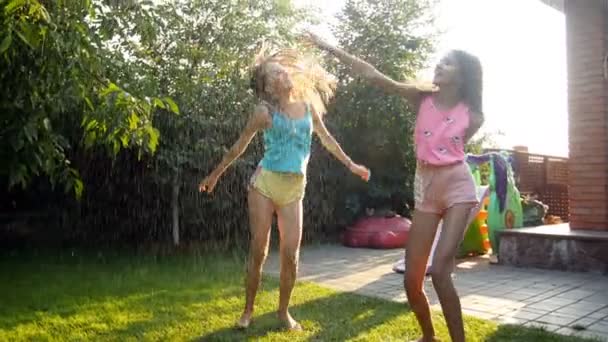 4k imagens de duas alegres garotas rindo adolescentes pulando e dançando sob a chuva no quintal da casa — Vídeo de Stock