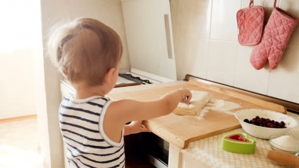 4 k beelden van schattige peuter jongen snijden deeg op een houten bord met ronde cutter mes — Stockvideo