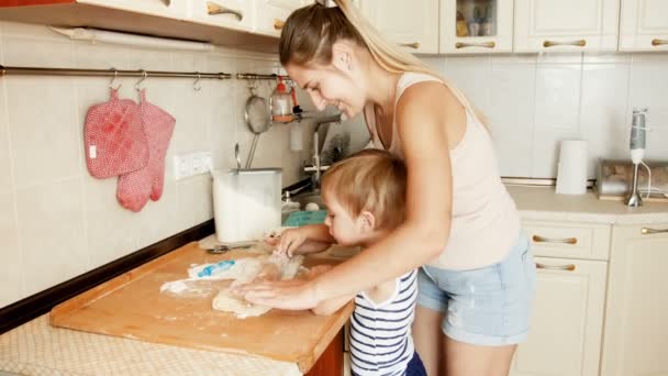 4k видео милого малыша, помогающего матери катить тесто за пирогом на кухне — стоковое видео
