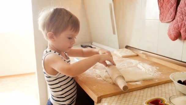 4k video of funny toddler boy rolling pie dough with big wooden rolling pin on kitchen countertop — Stock Video