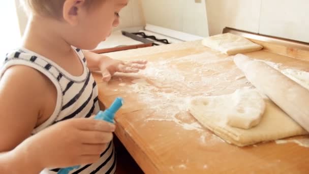 Gros plan vidéo 4k de petit garçon saupoudrer la pâte à tarte avec de la farine sur la table de cuisson de la cuisine — Video