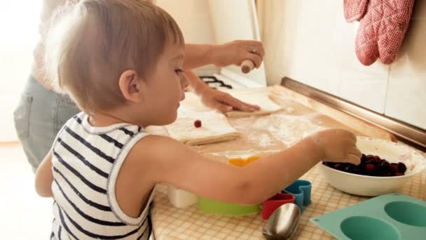 4k відео маленького малюка хлопчика, який допомагає мамі готувати пиріг і класти вишні в тісто — стокове відео