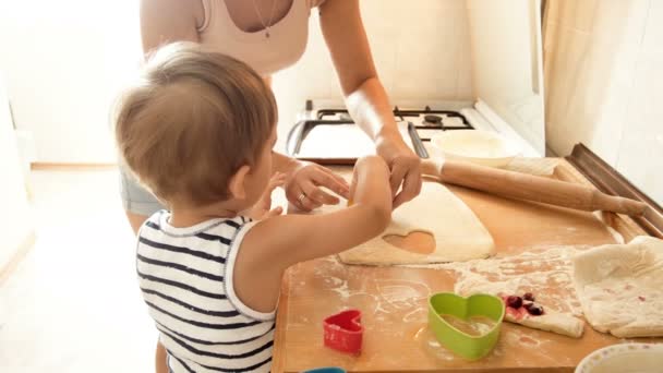 4k Filmmaterial von der jungen Mutter, die ihrem kleinen Sohn beibringt, Teig für Kekse mit speziellen Plastikausstechern zu schneiden — Stockvideo