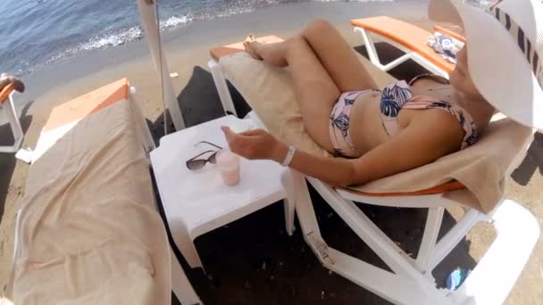 4k vídeo de bela jovem mulher de chapéu relaxante na praia e beber coquetel — Vídeo de Stock