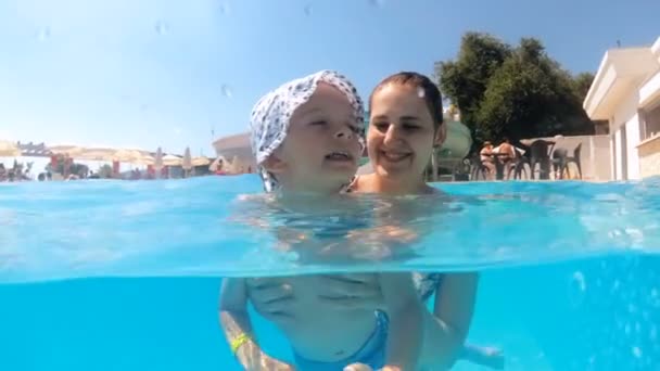 Vídeo em câmera lenta de uma jovem sorridente feliz com seu filho na piscina no resort do hotel — Vídeo de Stock