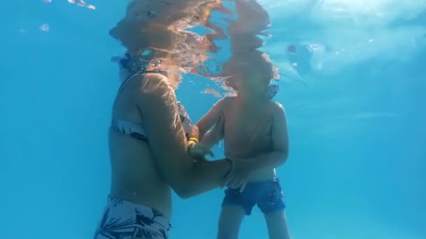 Zeitlupen-Unterwasser-Video von kleinem Kleinkind, das mit Mutter bei sonnigem Wetter schwimmt — Stockvideo