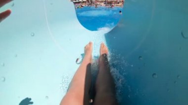 Aquapark 'ta su kaydırağına binen ve yüzme havuzunda suya düşen genç adamın yavaş çekim POV videosu.