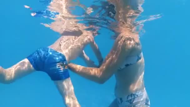 Повільний рух під водою відео молодої матері, що підтримує свого маленького сина, який плаває в басейні в сонячний день — стокове відео
