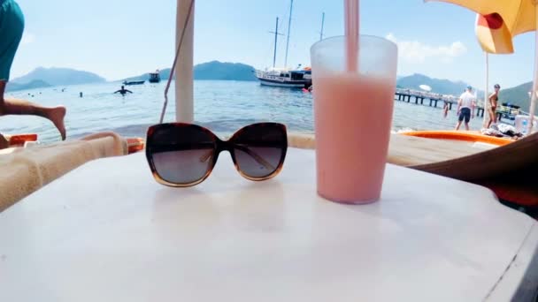 Primo piano video al rallentatore di cocktail e occhiali da sole sul tavolo sulla spiaggia in mare — Video Stock