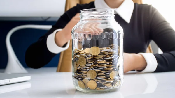 Photo rapprochée de jeune femme d'affaires au bureau avec pot en verre plein de pièces de monnaie — Photo