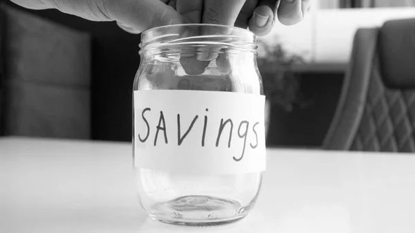 Primer plano imagen en blanco y negro de un par de manos poniendo moneda en frasco con ahorros de dinero de la familia — Foto de Stock
