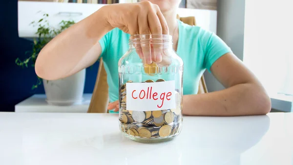 Foto close-up de jovem mulher jogando dinheiro em frasco de vidro com poupança para a educação na faculdade — Fotografia de Stock