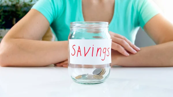 Closeup photo of young woman sitting with glass jar for savings with few coins — Stock Photo, Image