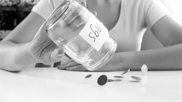 Imagen en blanco y negro de una mujer joven vertiendo monedas de un frasco de vidrio con ahorros — Foto de Stock