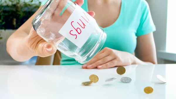 特写照片的年轻女子倒硬币的玻璃罐子与节省金钱 — 图库照片