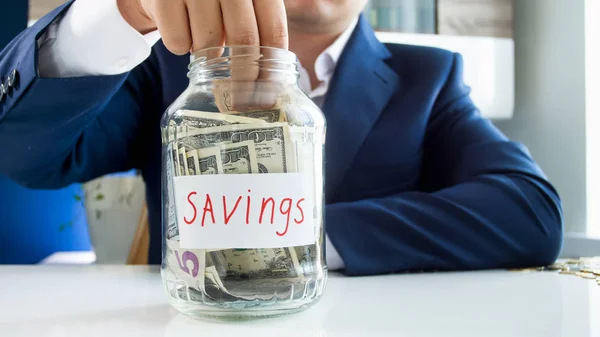 Foto conceptual de ahorrar dinero. Empresario llenando frasco de vidrio con billetes de dólar — Foto de Stock