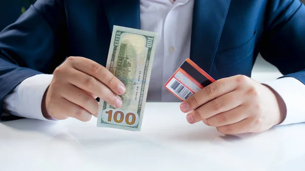 Imagen de primer plano del empresario dudando del uso de billetes con tarjeta de crédito o papel moneda tradicional —  Fotos de Stock