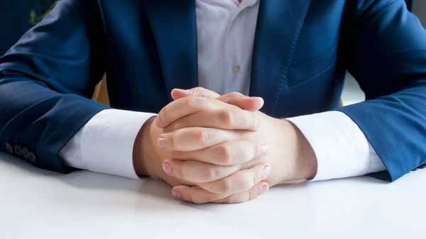Közelkép kép fiatal üzletember, összekulcsolt kézzel mögött fehér fa íróasztal hivatalban ülve kék színben — Stock Fotó