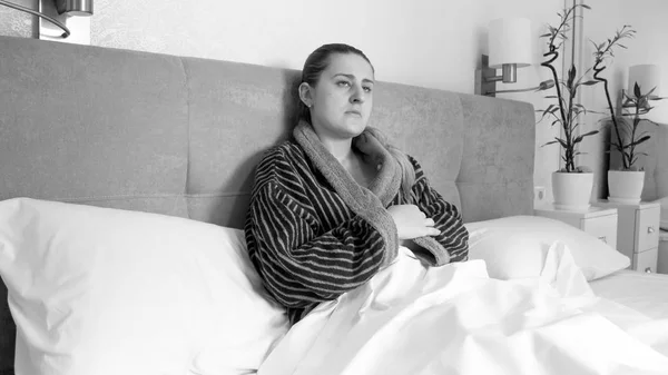 Imagen en blanco y negro de una mujer deprimida en albornoz acostada en la cama en casa — Foto de Stock